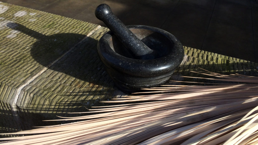 Mort and pestle with palm ashes and dried palm leaves on a table.