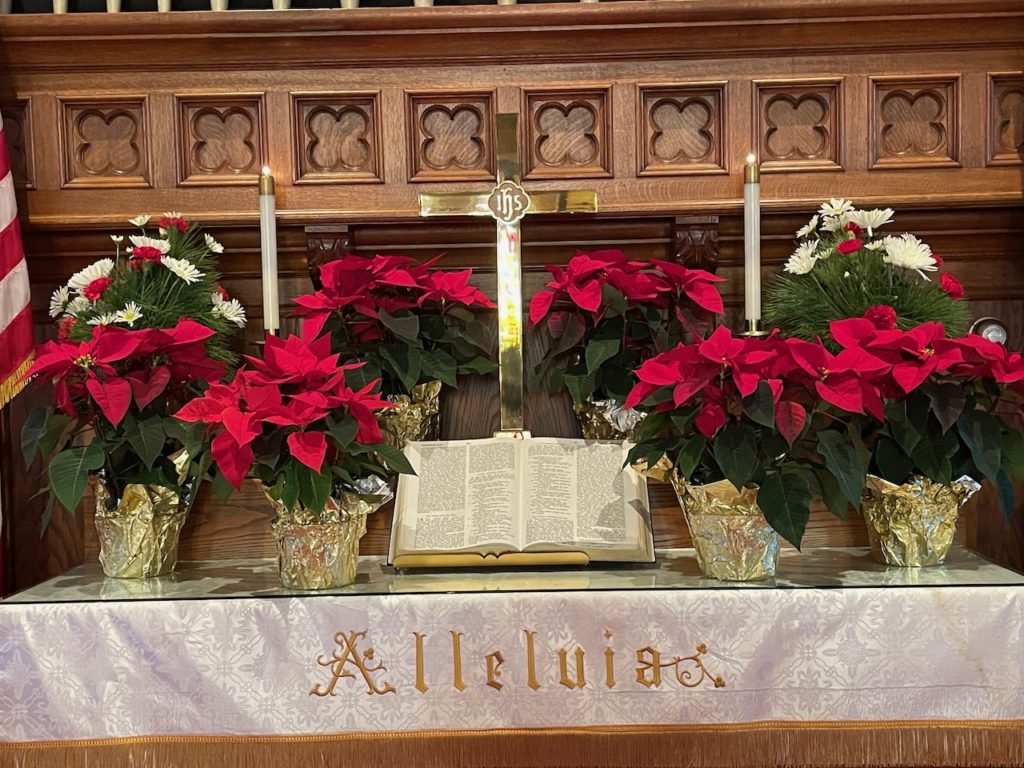 Poinsettias on the altar with candles lit, a cross, and a Bible opened