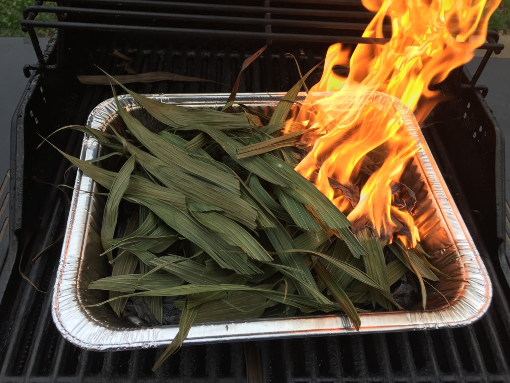 Dried palms in a container on a grill being set on fire.
